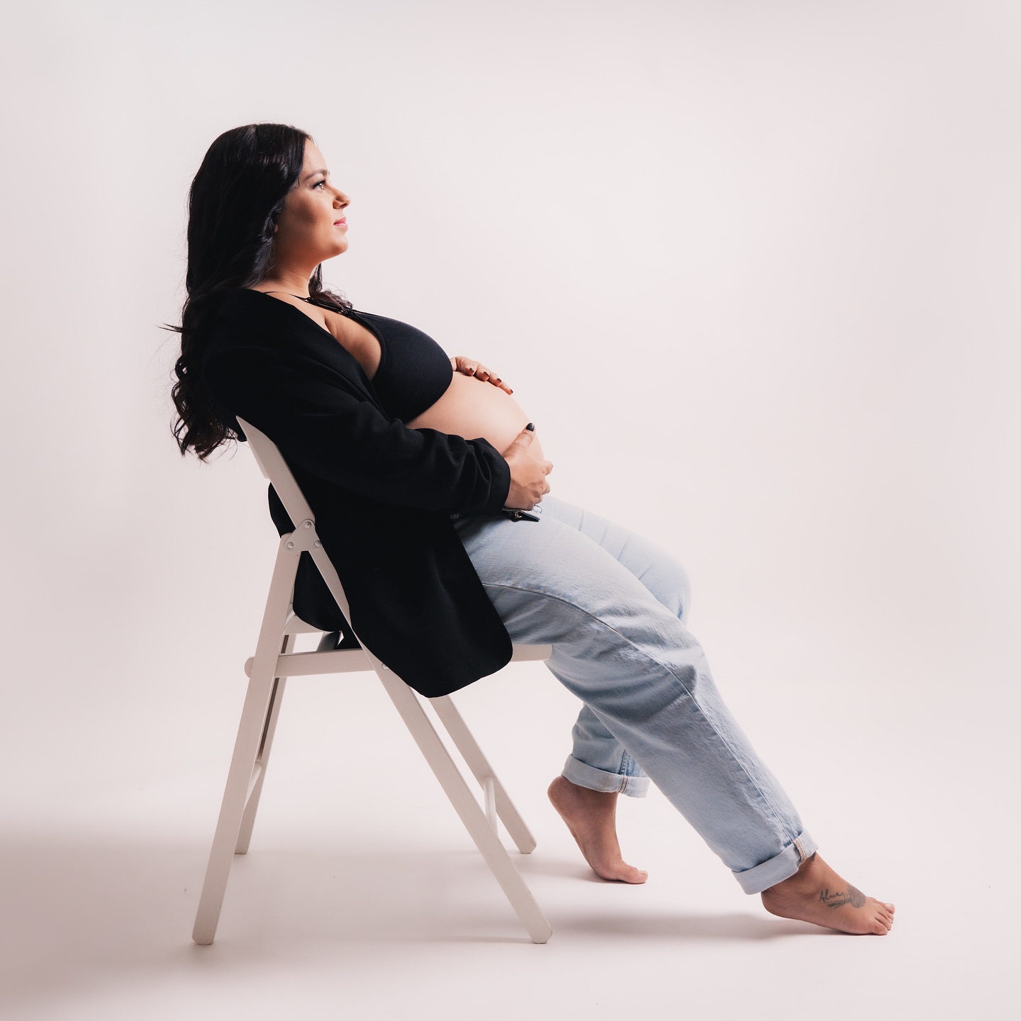 Mujer embarazada sentada elegantemente en una silla, acariciando su vientre.